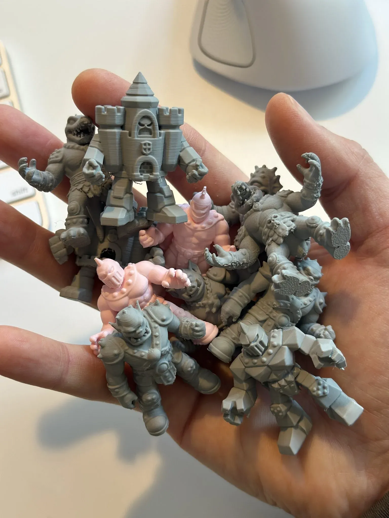 About ten small 3D-printed toy figures, most in gray and two in pink, piled in an open hand.