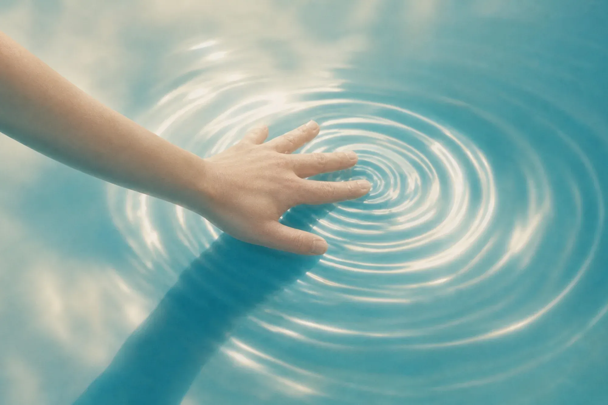 The same hand and rings on turquoise water with sky reflected in it.
