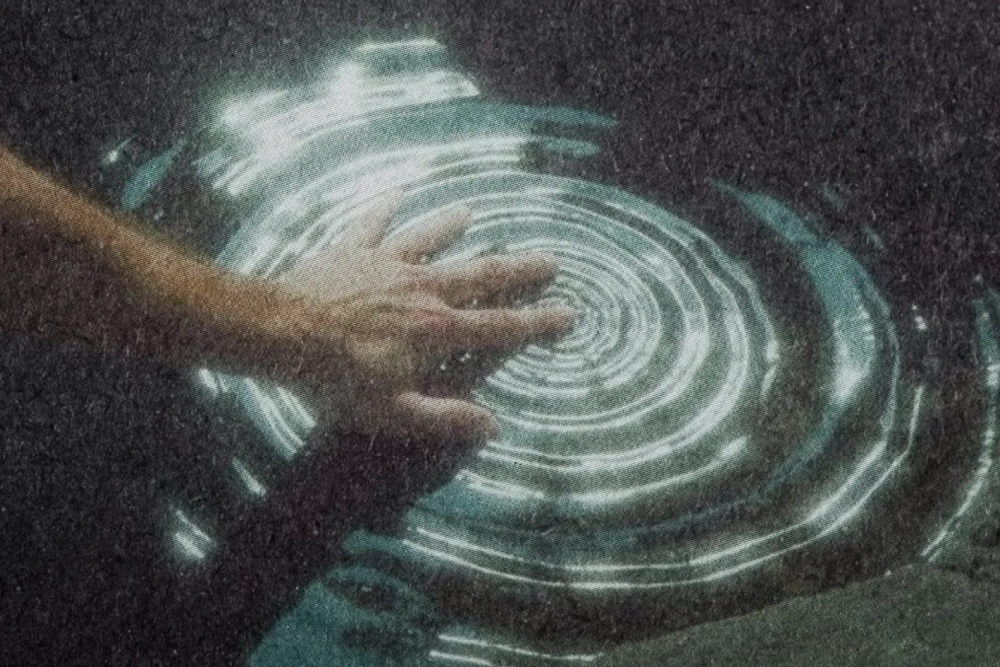 A hand touching dark water in a rock pool, with bright rings spreading from the fingers.